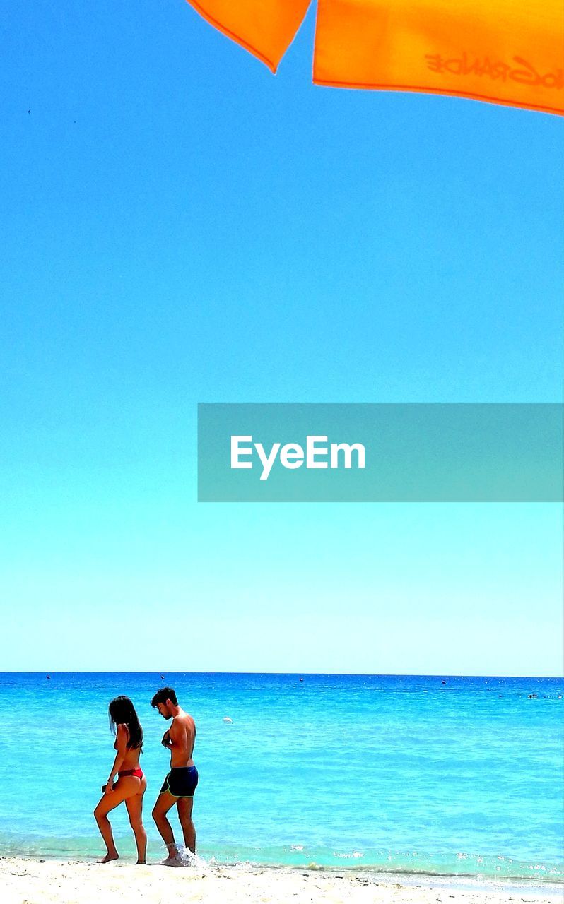 FRIENDS ON BEACH AGAINST CLEAR SKY