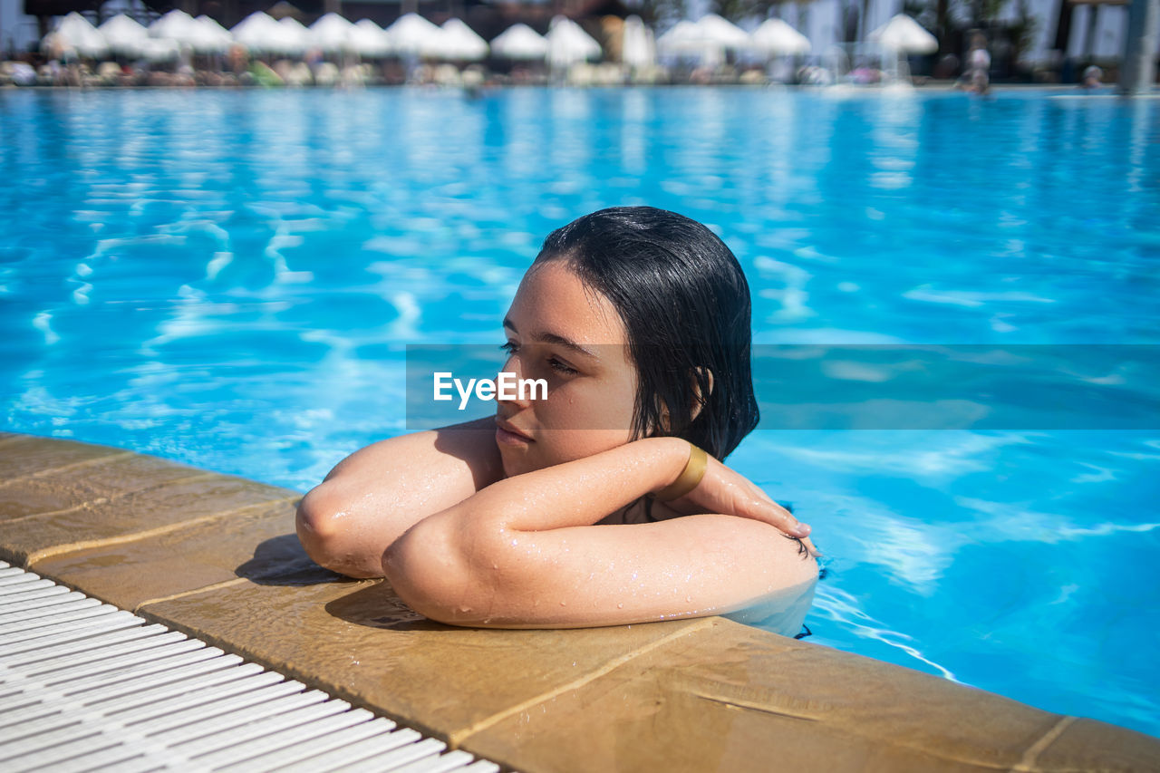 Young brunette teen girl posing in blue swimming pool in a hotel in turkey