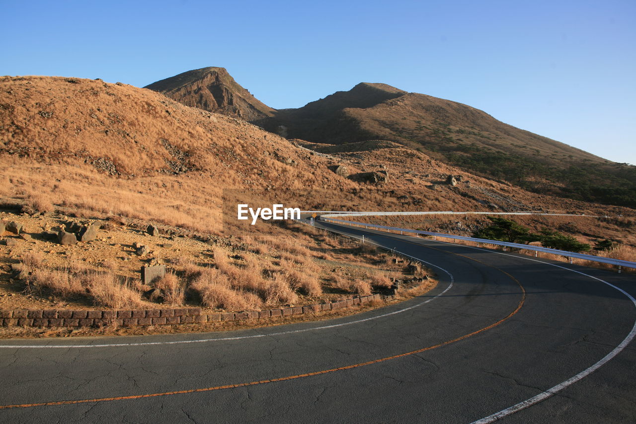 Road leading towards mountains against clear sky