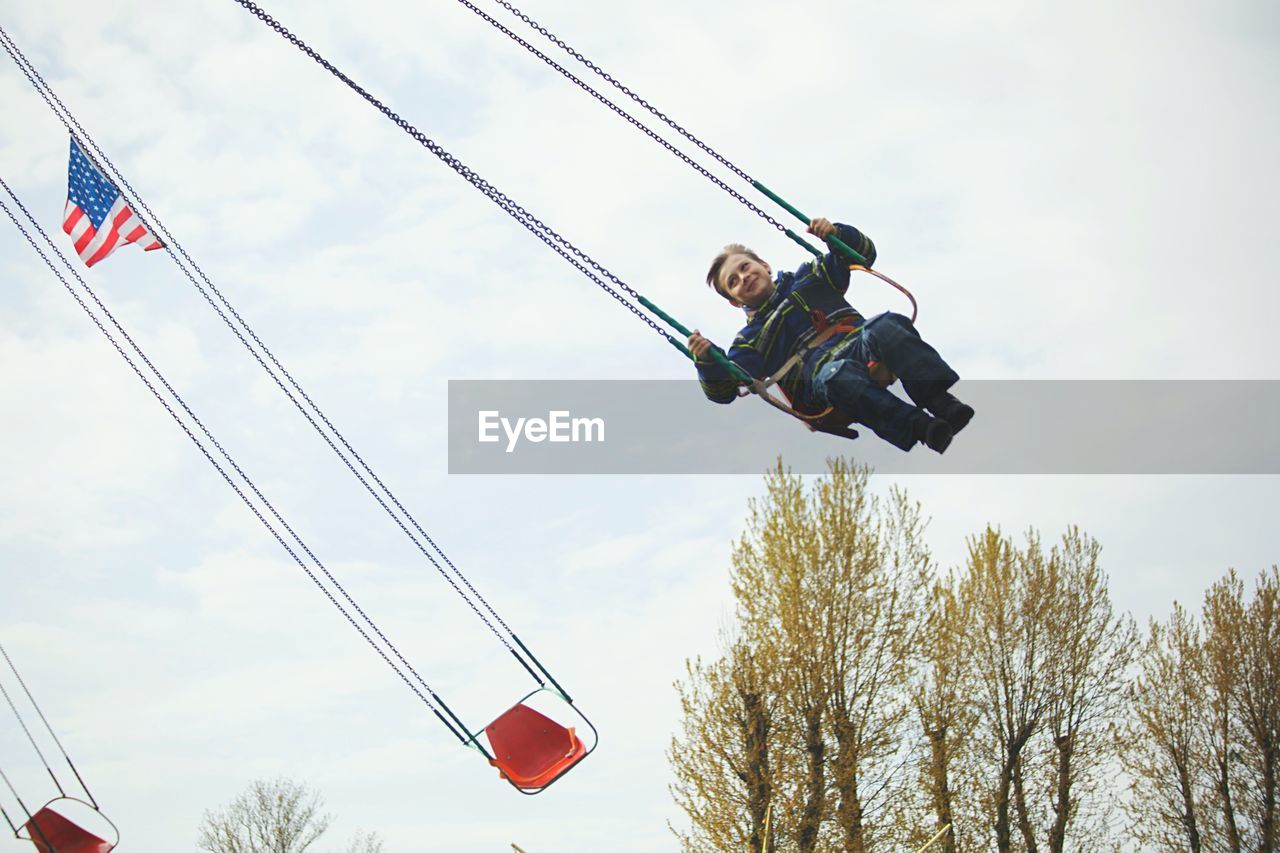 Low angle view of boy enjoying on chain swing ride against sky