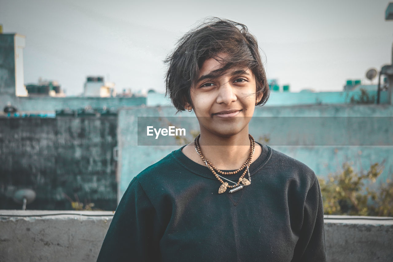 Portrait of smiling young woman standing against sky