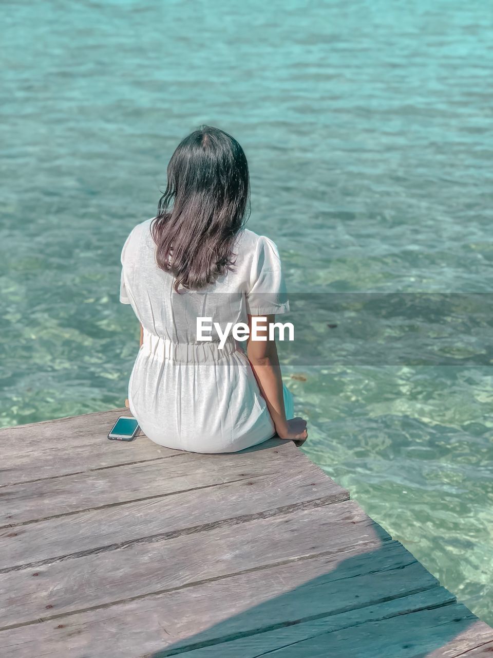 Rear view of woman sitting on pier over sea