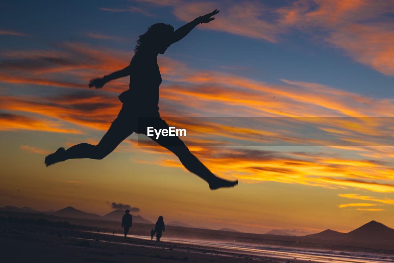 Silhouette people jumping on beach against sky during sunset