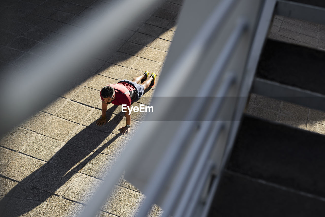High angle view of confident man doing push-ups on footpath in city