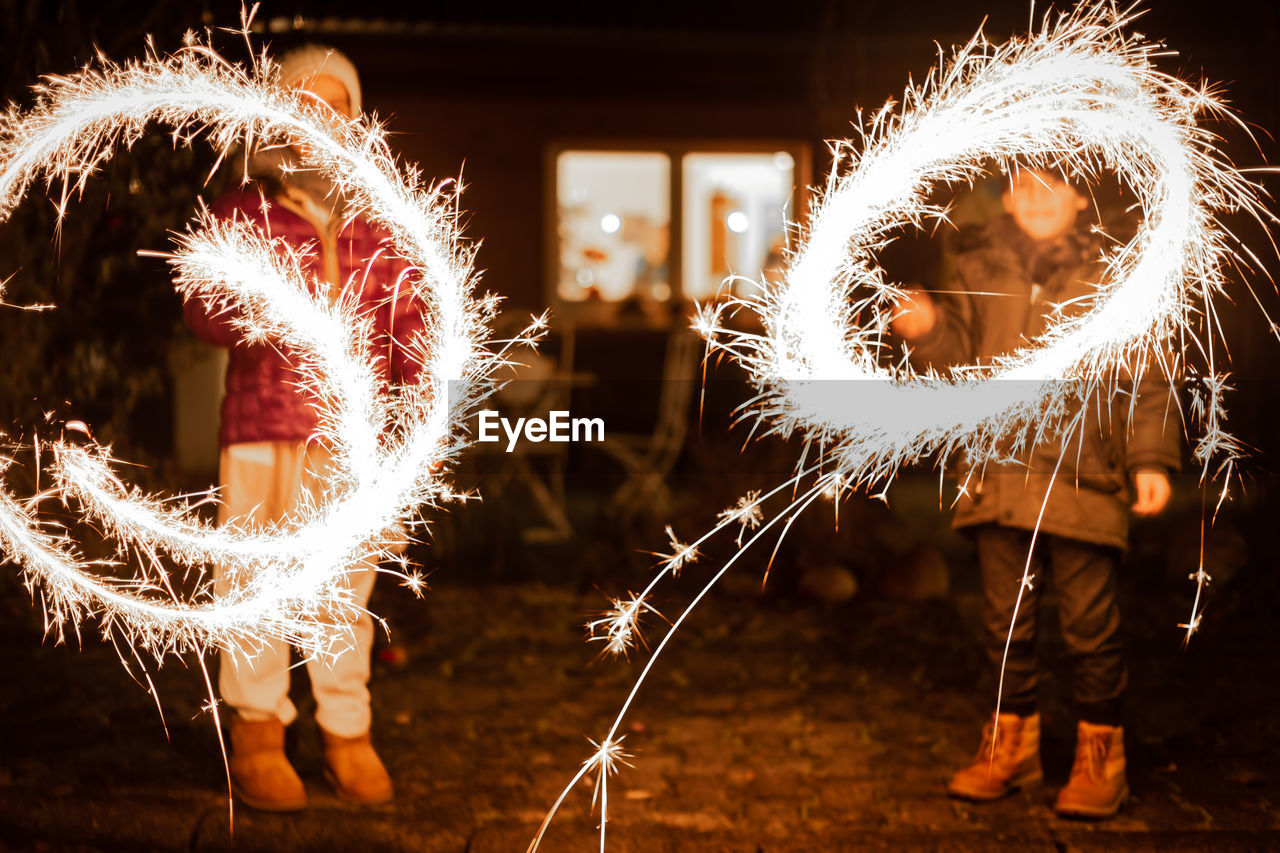 Siblings spinning wire wool while standing on land at night