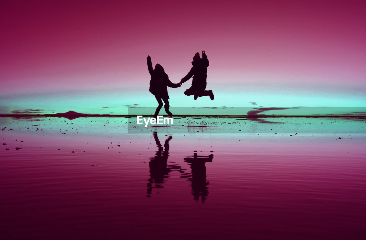 Pop art styled silhouette of happy couple jumping on the mirror effect of uyuni salt flats, bolivia