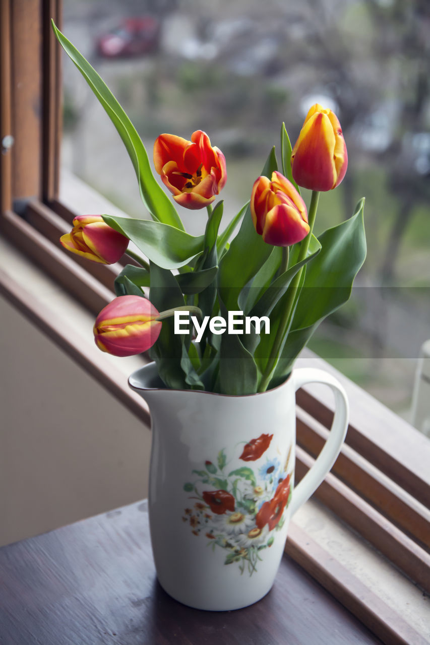 A white porcelain jug with flower print containing a bouquet of red and yellow tulips.