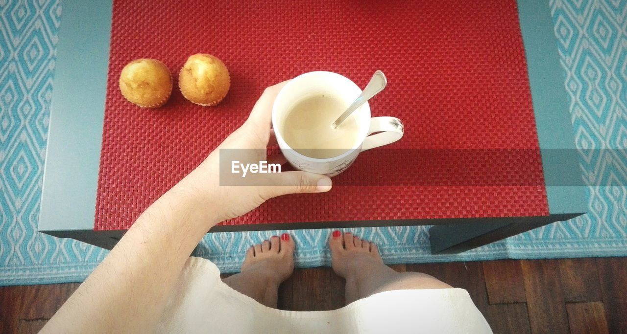 Low section of woman holding milk in cup by cupcakes on table