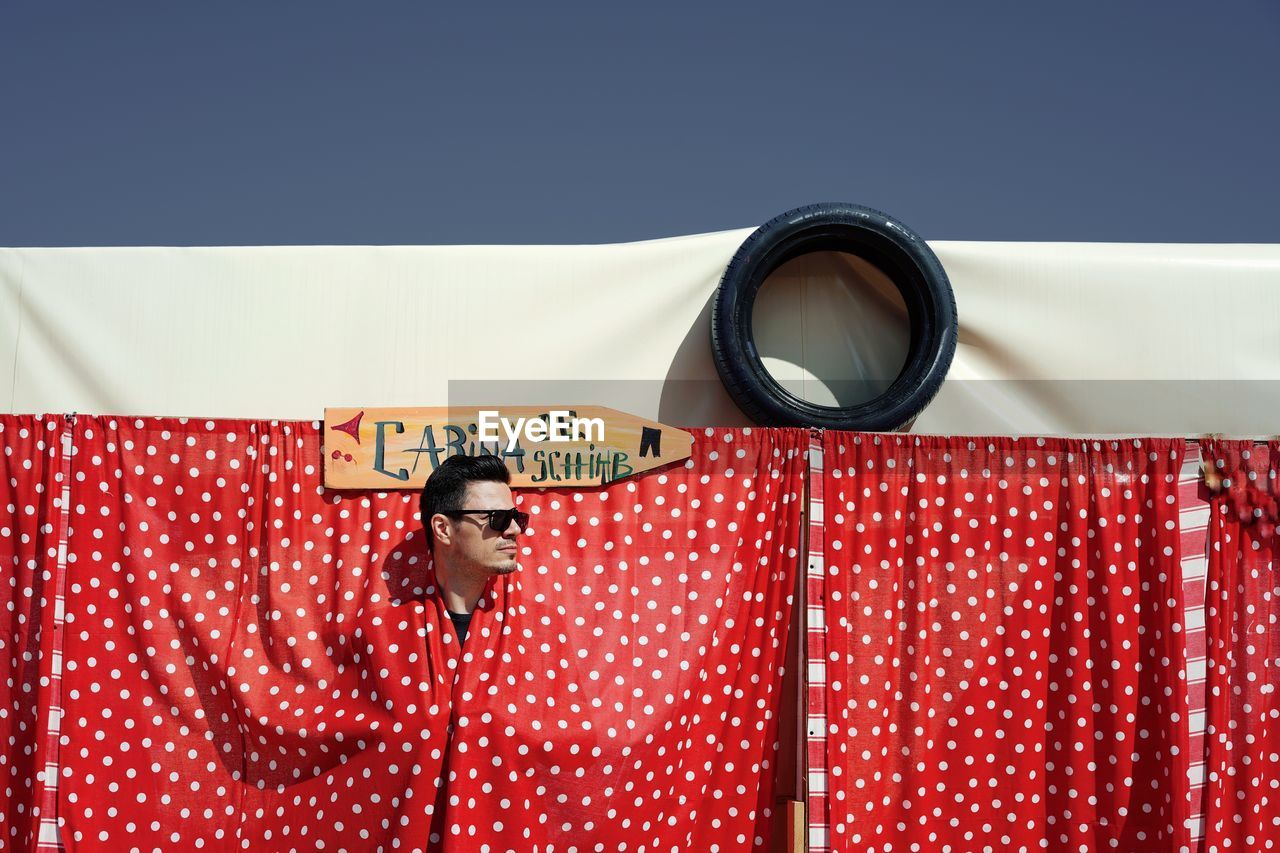 Man hiding behind red curtain against clear sky