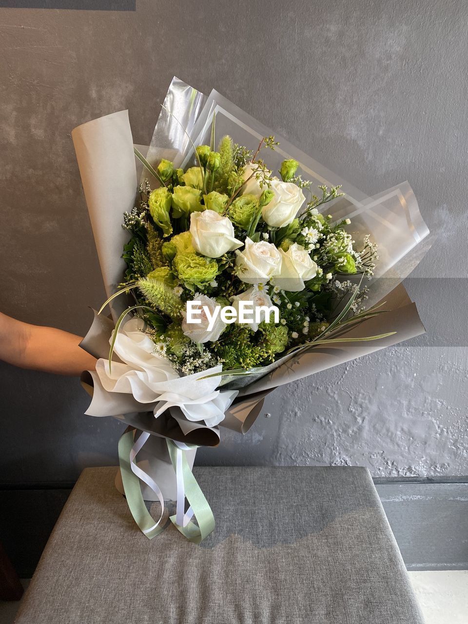 Cropped hand of woman holding flower bouquet against wall