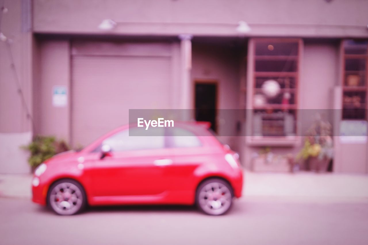Defocused image of red car parked on street against house