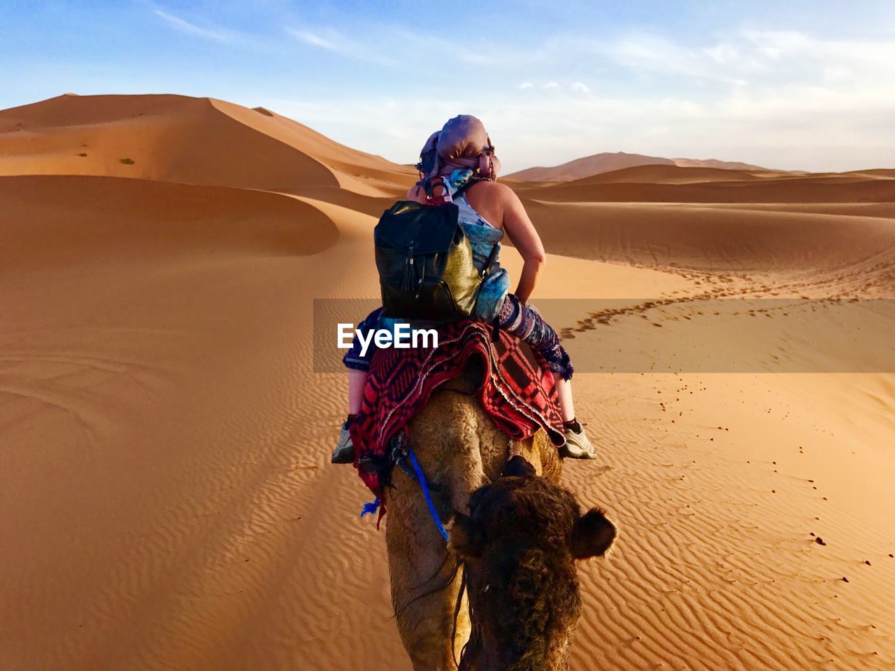 Rear view of woman riding camel at desert against sky