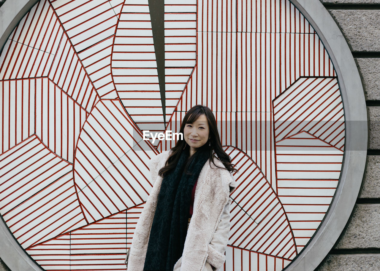 Portrait of young woman standing against patterned wall