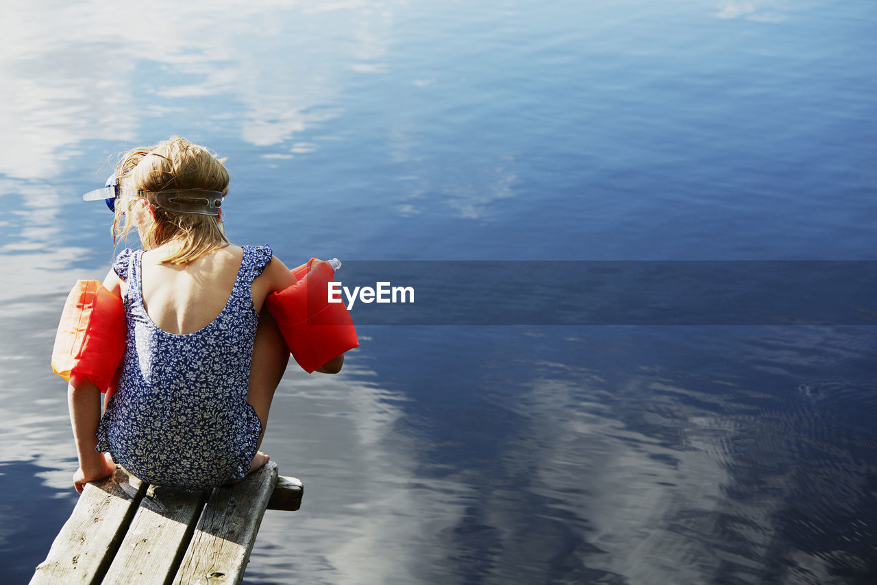 Girl sitting on jetty in water wings