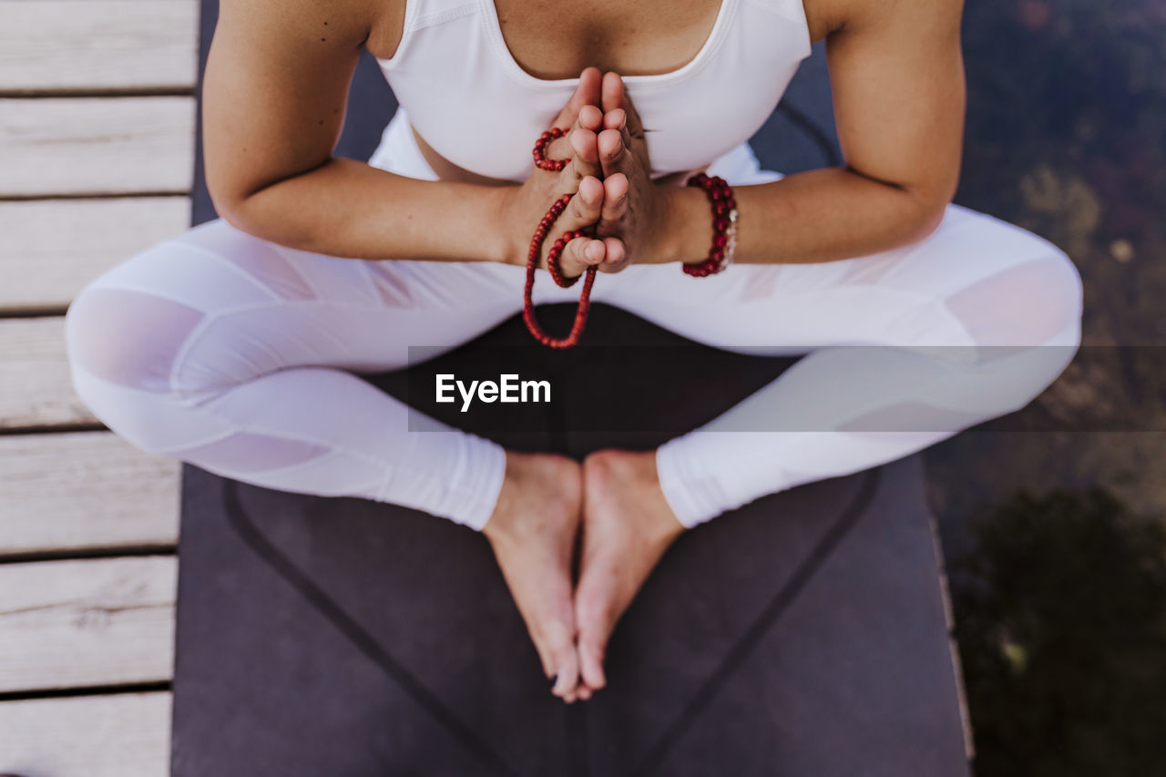 Low section of woman with hands clasped sitting on jetty