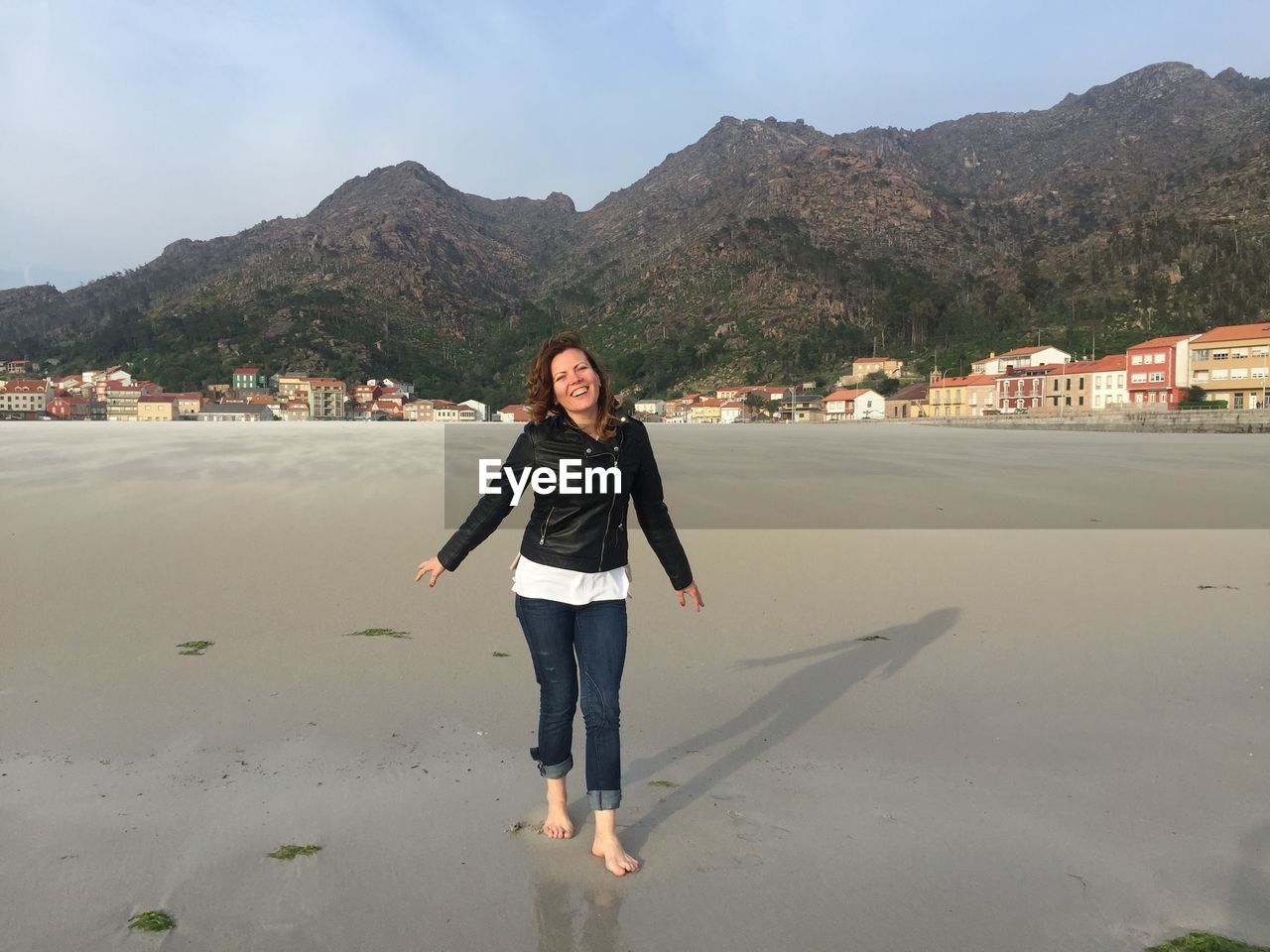 Portrait of smiling young woman standing on beach against sky