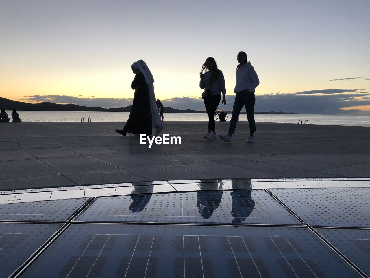 PEOPLE STANDING ON SHORE BY SEA AGAINST SKY