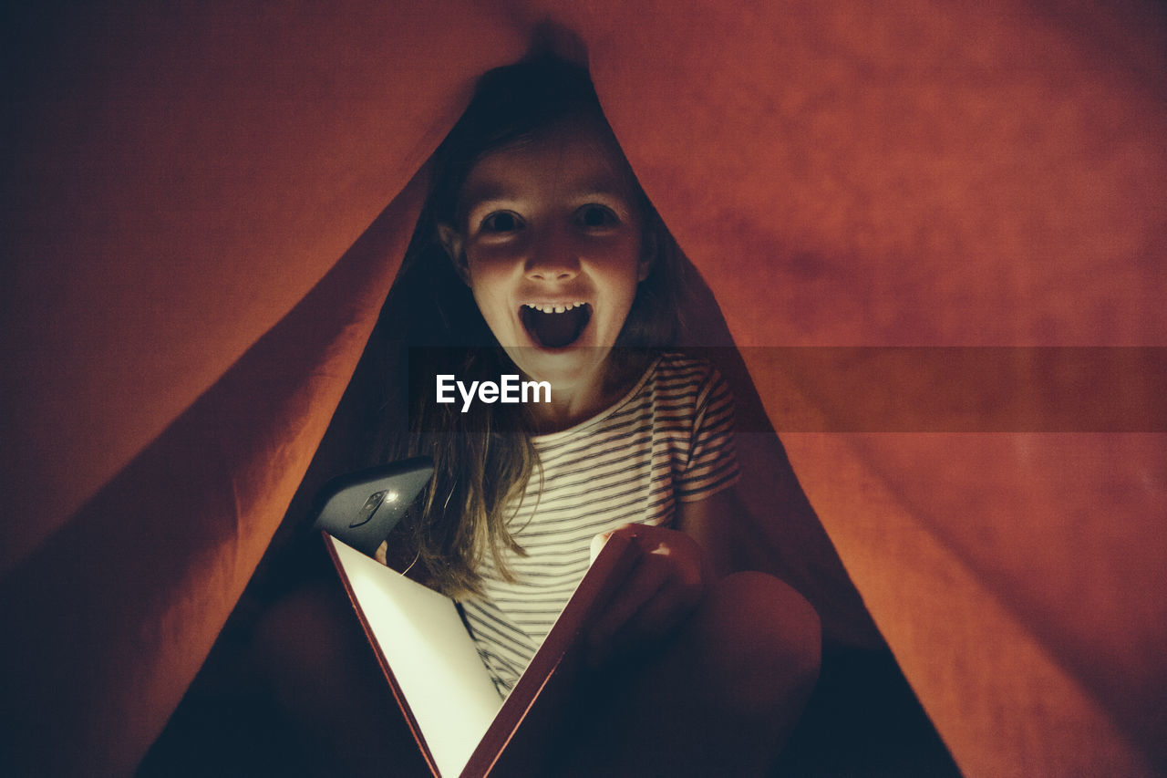 Portrait of excited girl holding mobile phone and book