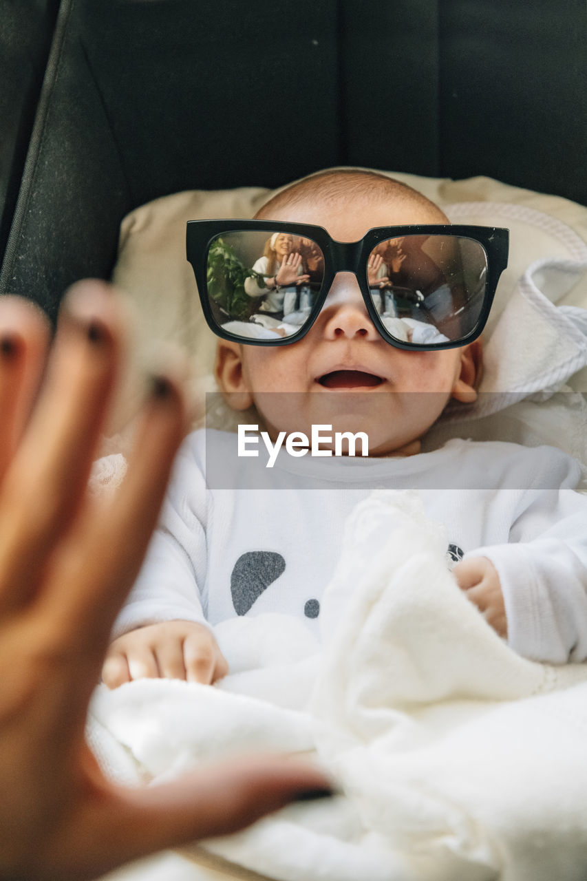 From above of newborn infant in pajama with open mouth in sun glasses lying on bed at home