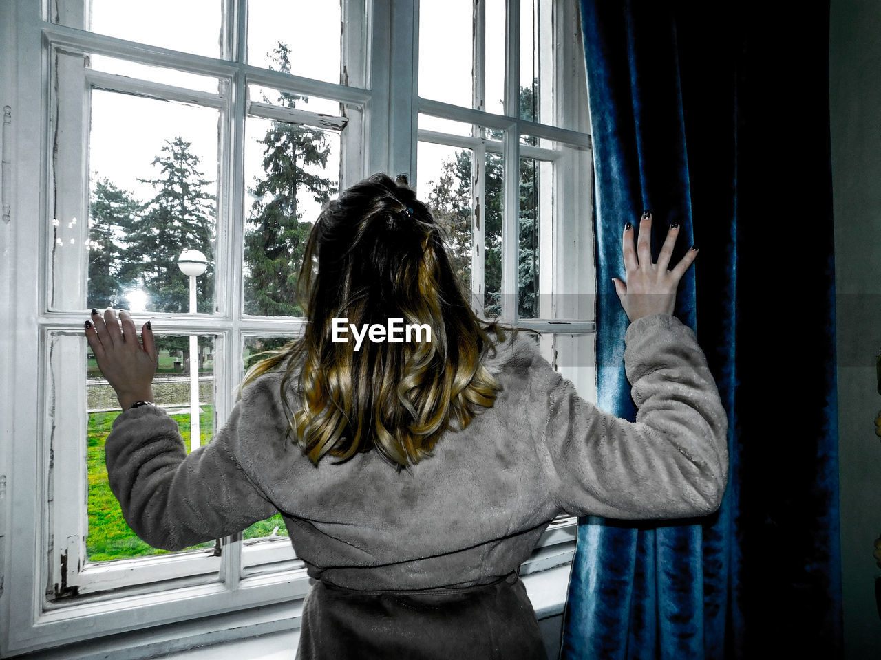 Rear view of woman standing against window at home