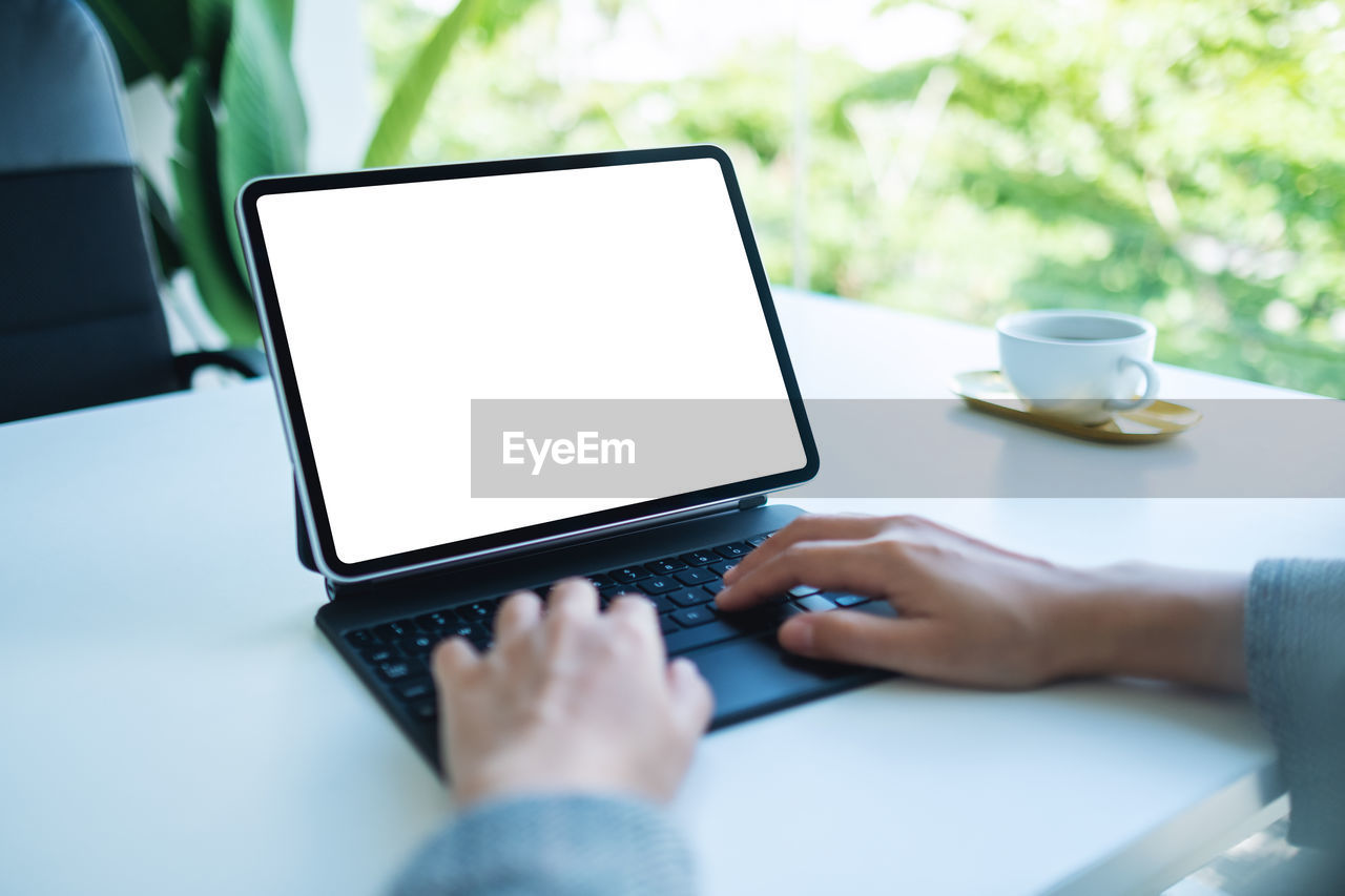 cropped hands of woman using laptop on table