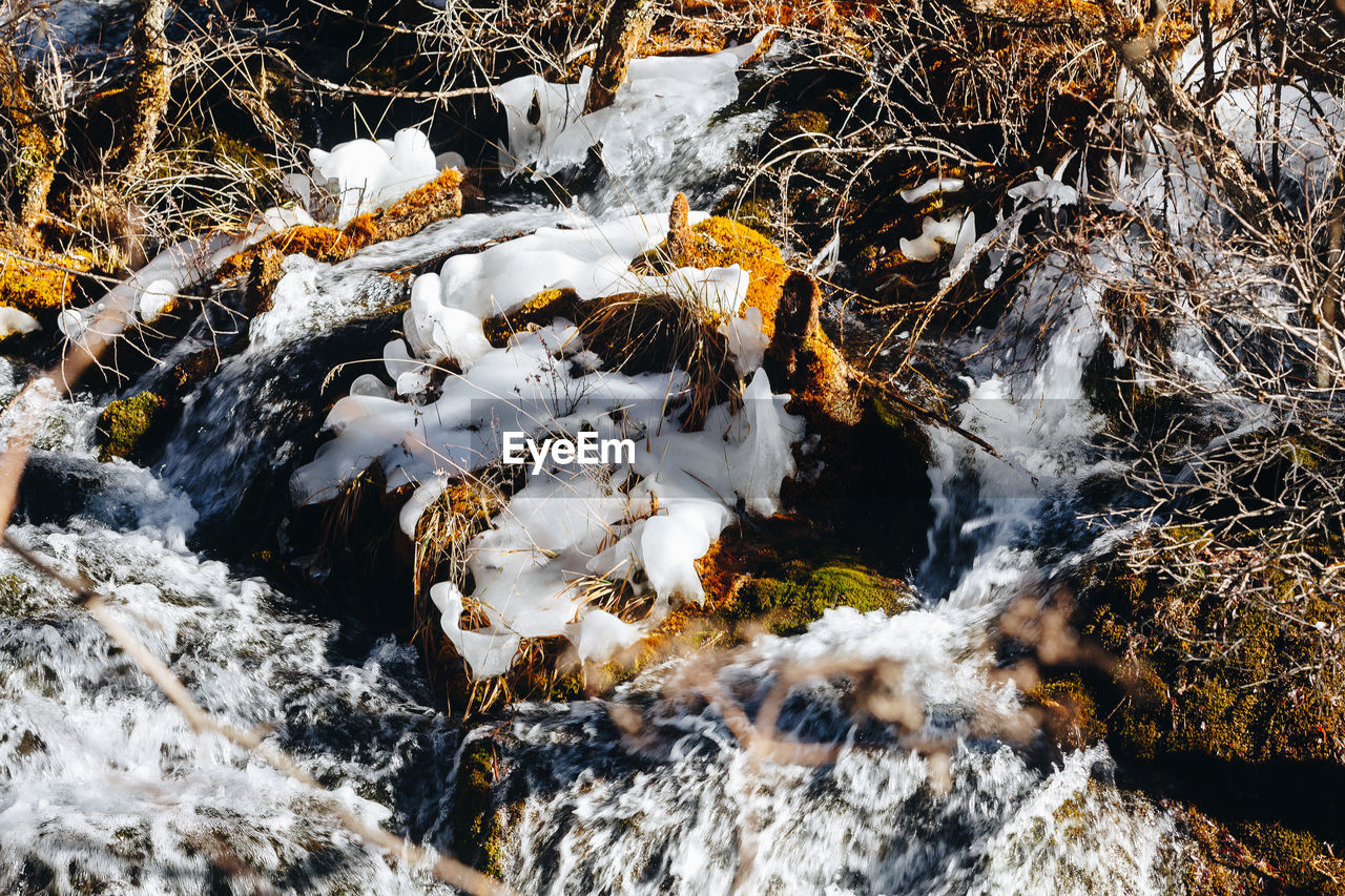 HIGH ANGLE VIEW OF STREAM FLOWING AMIDST ROCKS DURING WINTER