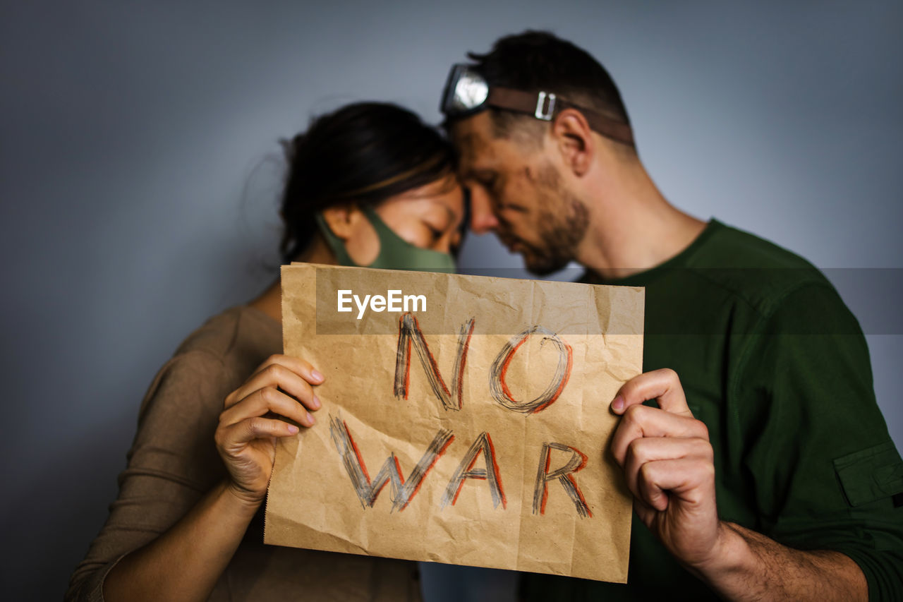 Upset couple homeless protesting war conflict raises banner with inscription message text no war. 