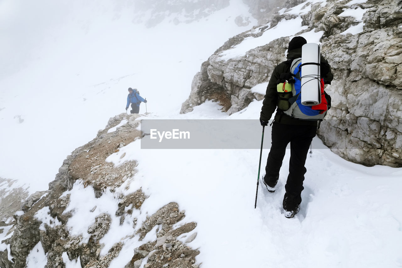 REAR VIEW OF PEOPLE WALKING ON SNOW COVERED MOUNTAINS