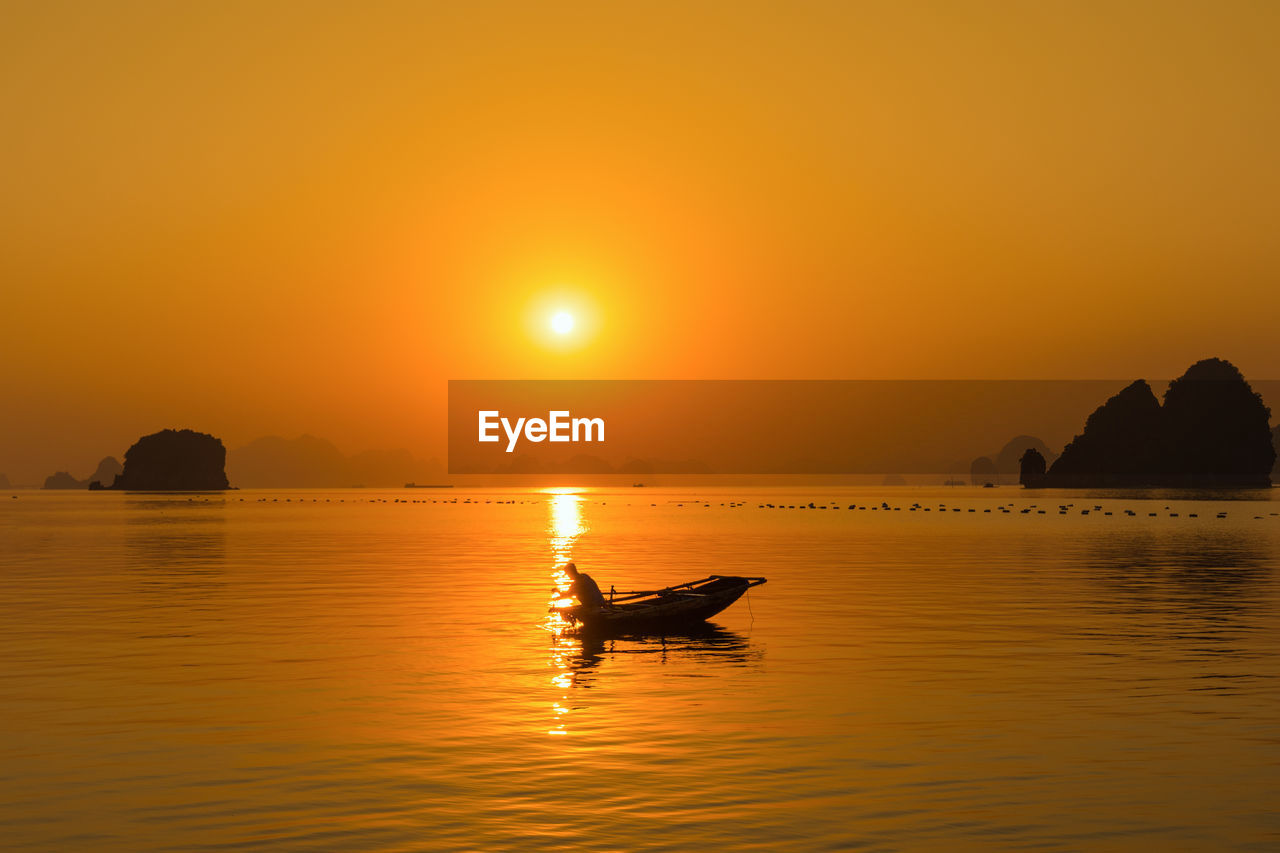 Silhouette boat in sea against orange sky