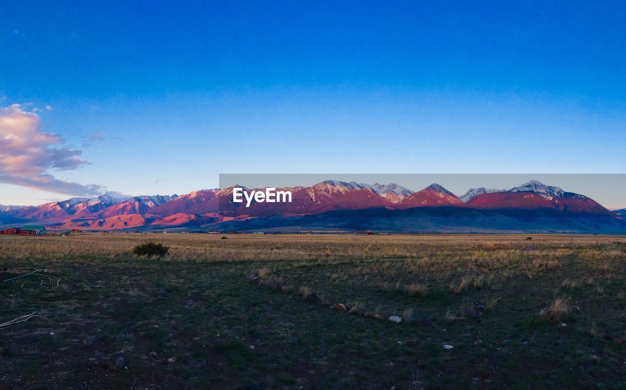 Scenic view of field and mountains against blue sky