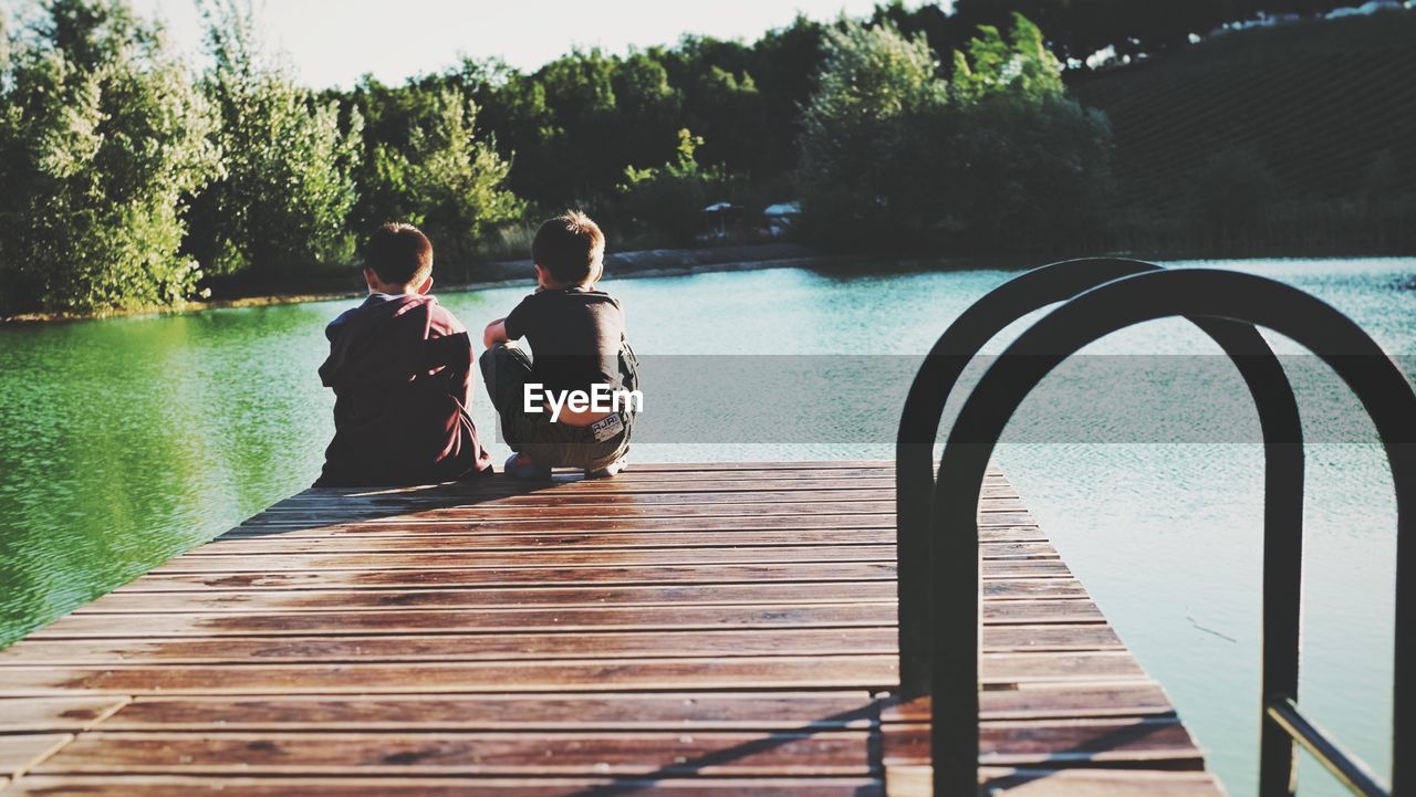 Rear view of siblings on pier over lake