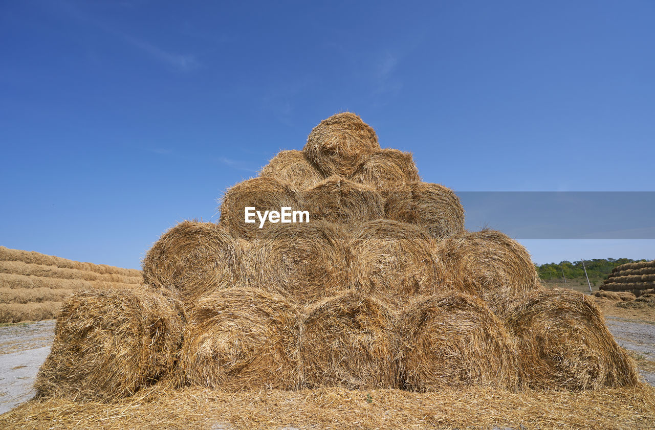 Hay bales on field against blue sky