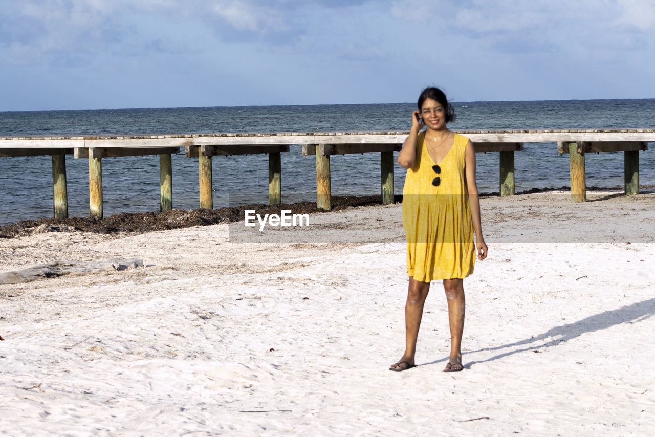 Full length of smiling woman standing at beach