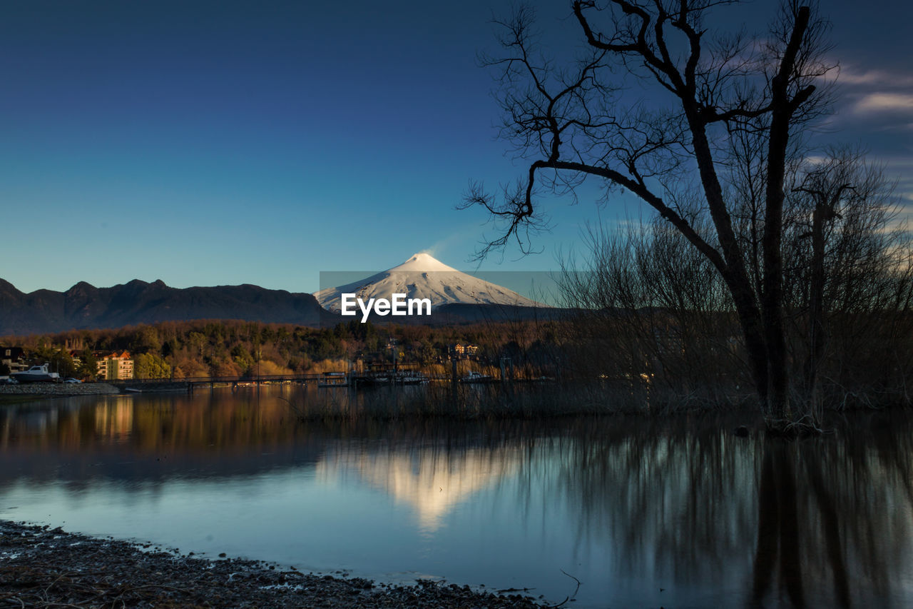 Scenic view of lake by trees against clear blue sky