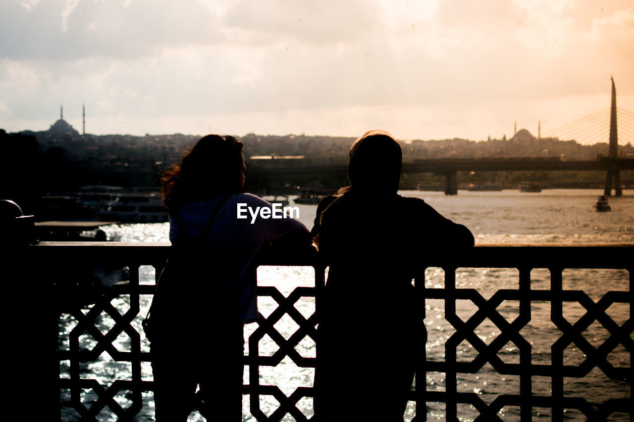 REAR VIEW OF SILHOUETTE MAN LOOKING AT VIEW OF RIVER