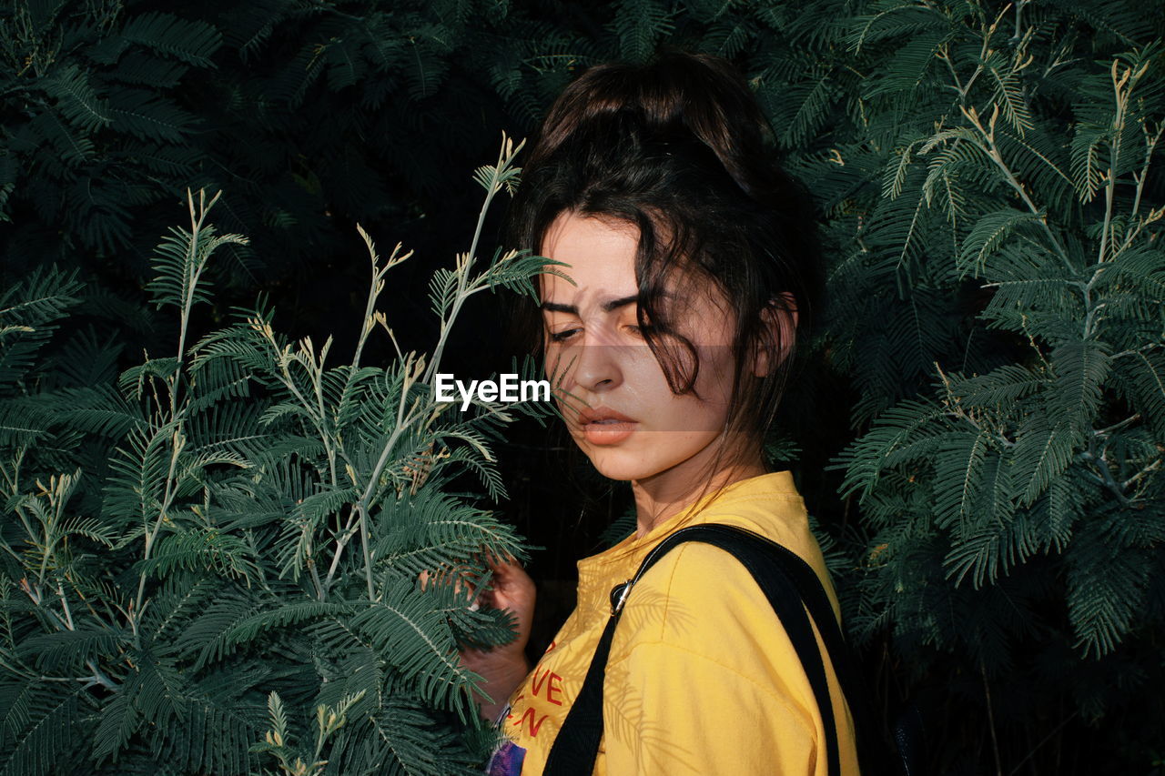 Thoughtful young woman standing amidst plants at night