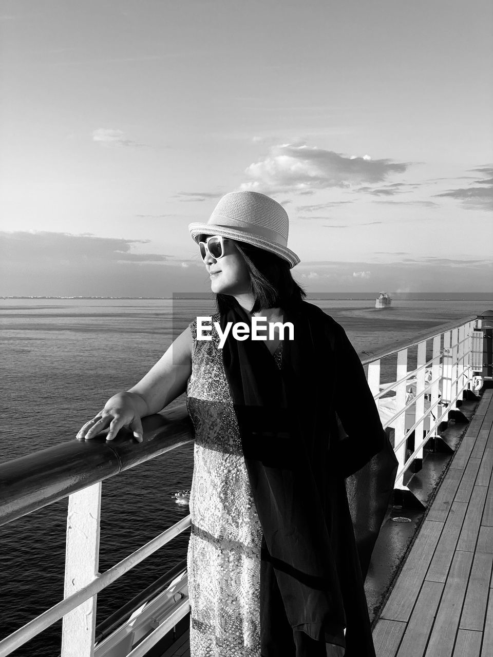 Woman wearing sunglasses while standing by railing of boat in sea against sky
