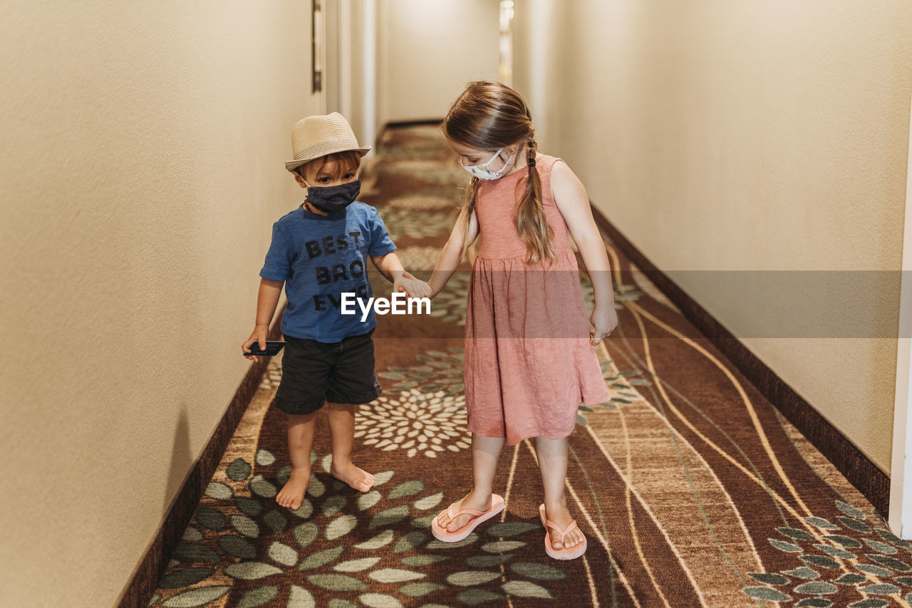 Young siblings wearing masks walking through hotel hallway together