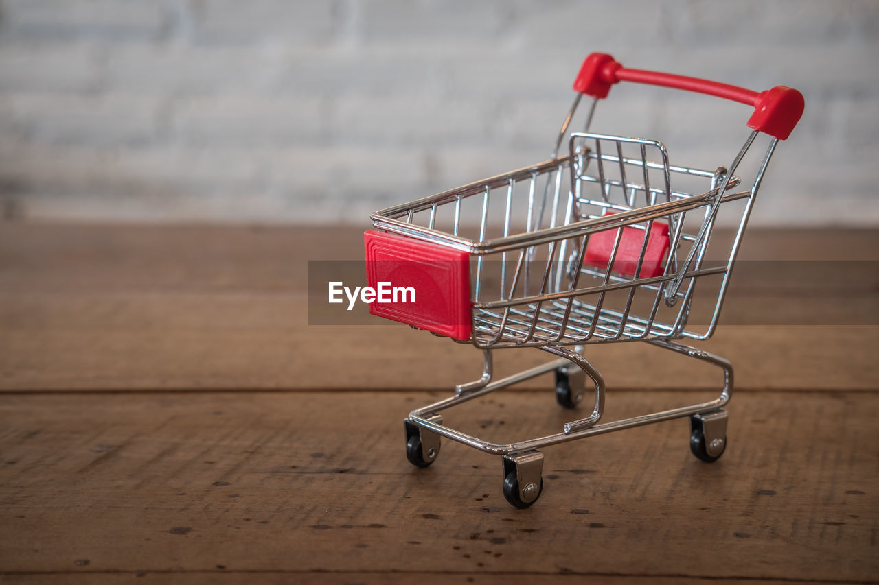 Close-up of small shopping cart on wooden table against wall