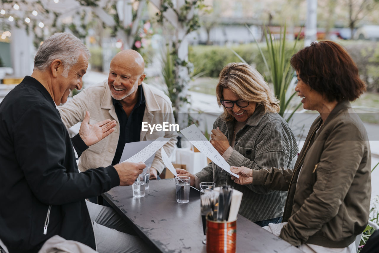 Happy male and female senior friends enjoying while reading menu card at restaurant