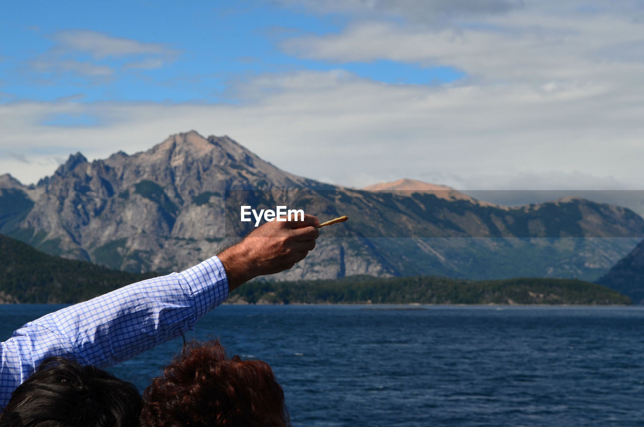 Cropped image of man with hand raised against river and mountains