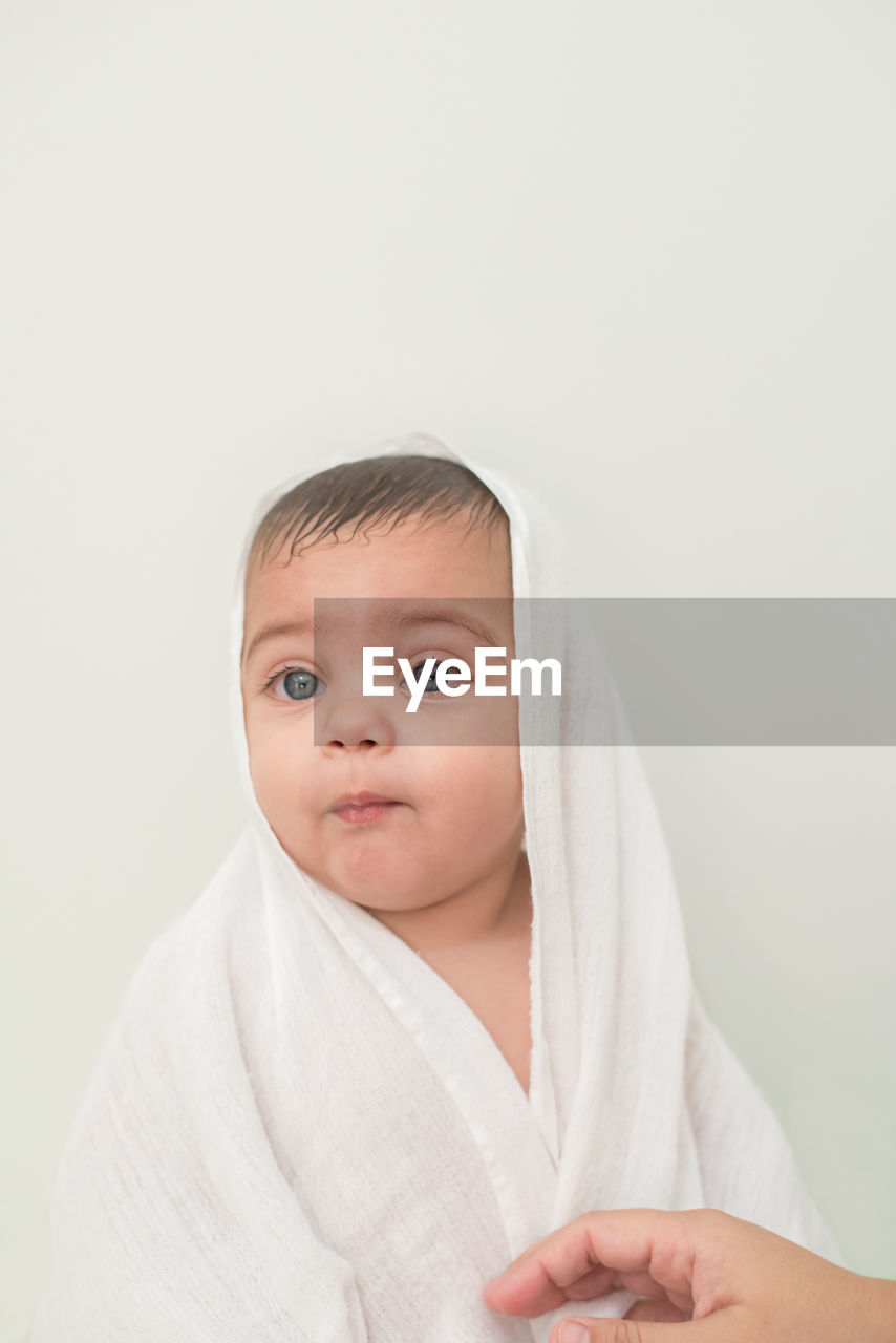 Thoughtful cute baby boy wrapped in towel while sitting against wall