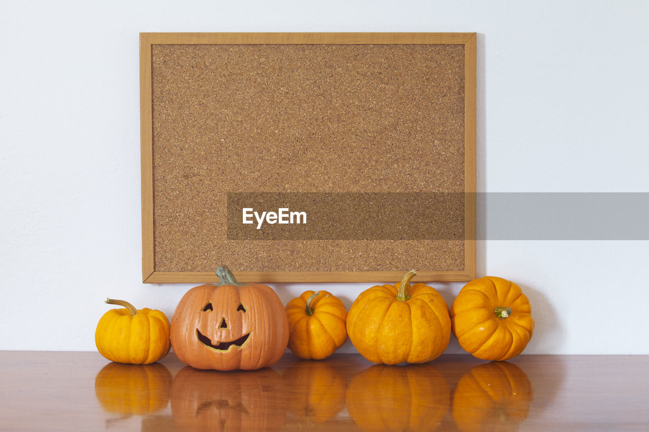 Jack o lantern and pumpkins against bulletin board on wall