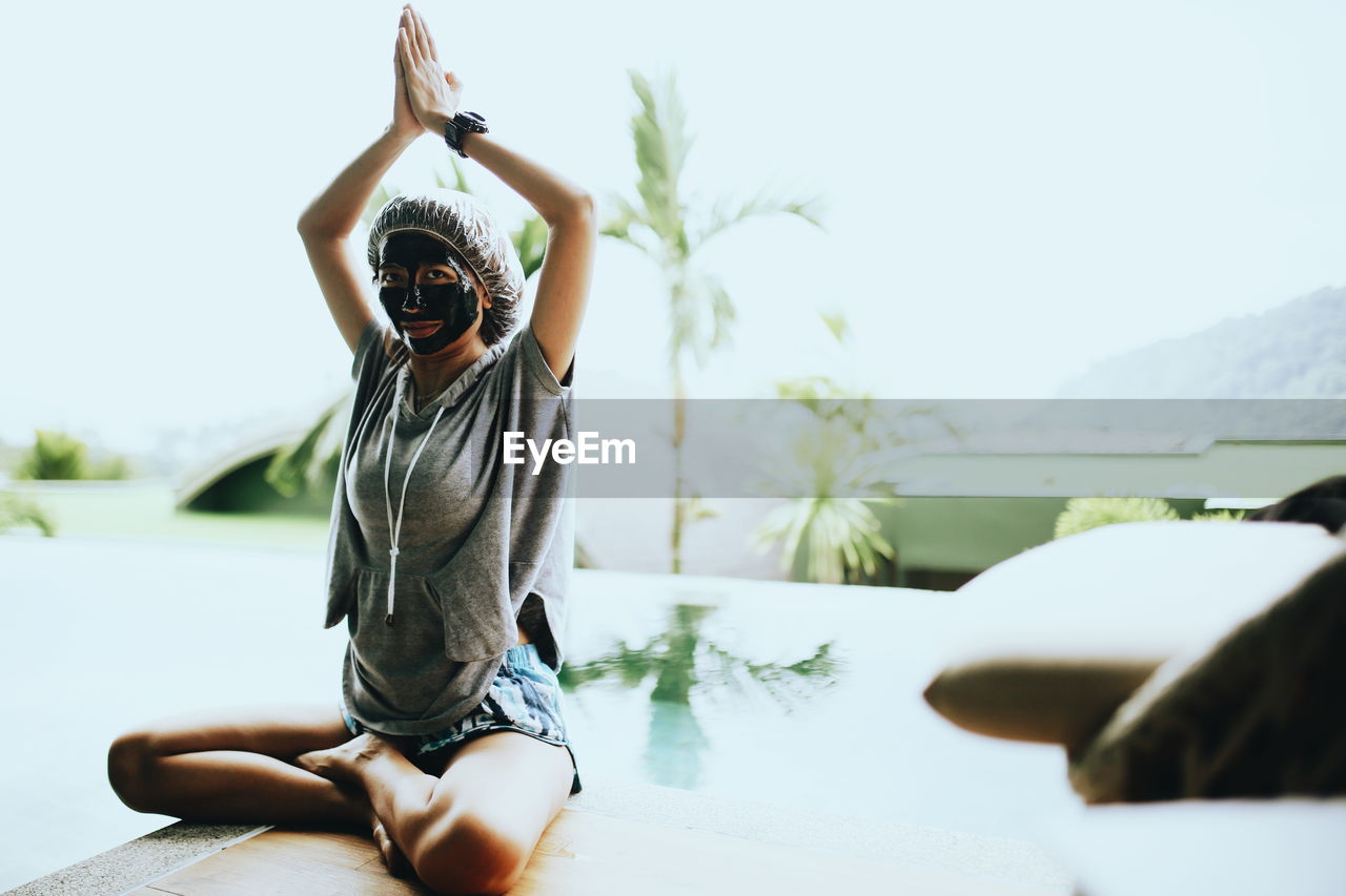 Portrait of woman wearing facial mask while doing yoga against sky