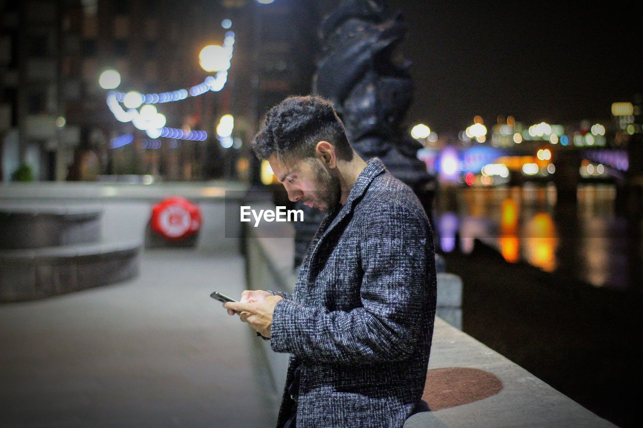 Side view of man using mobile phone in city at night
