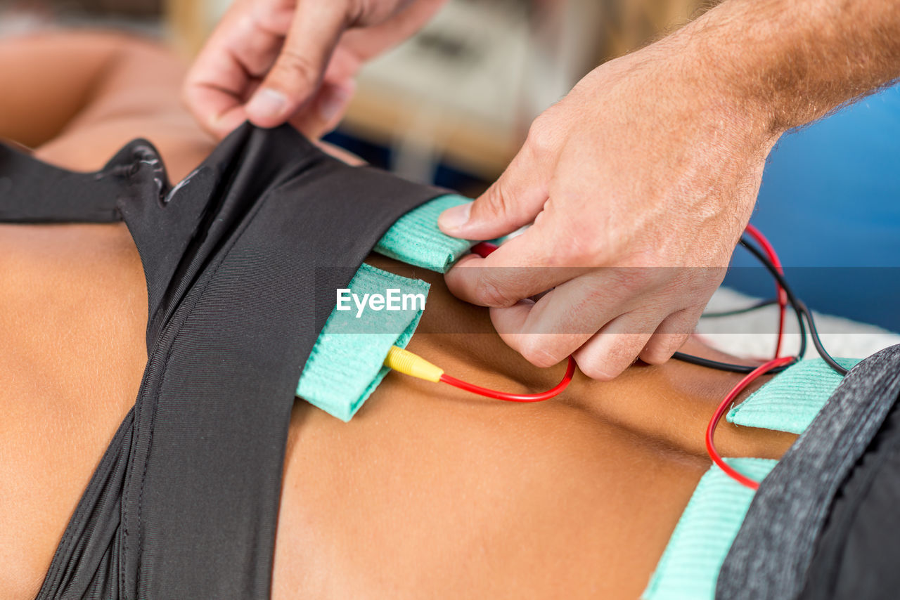 Midsection of physical therapist using electrical stimulation on womans back for treatment