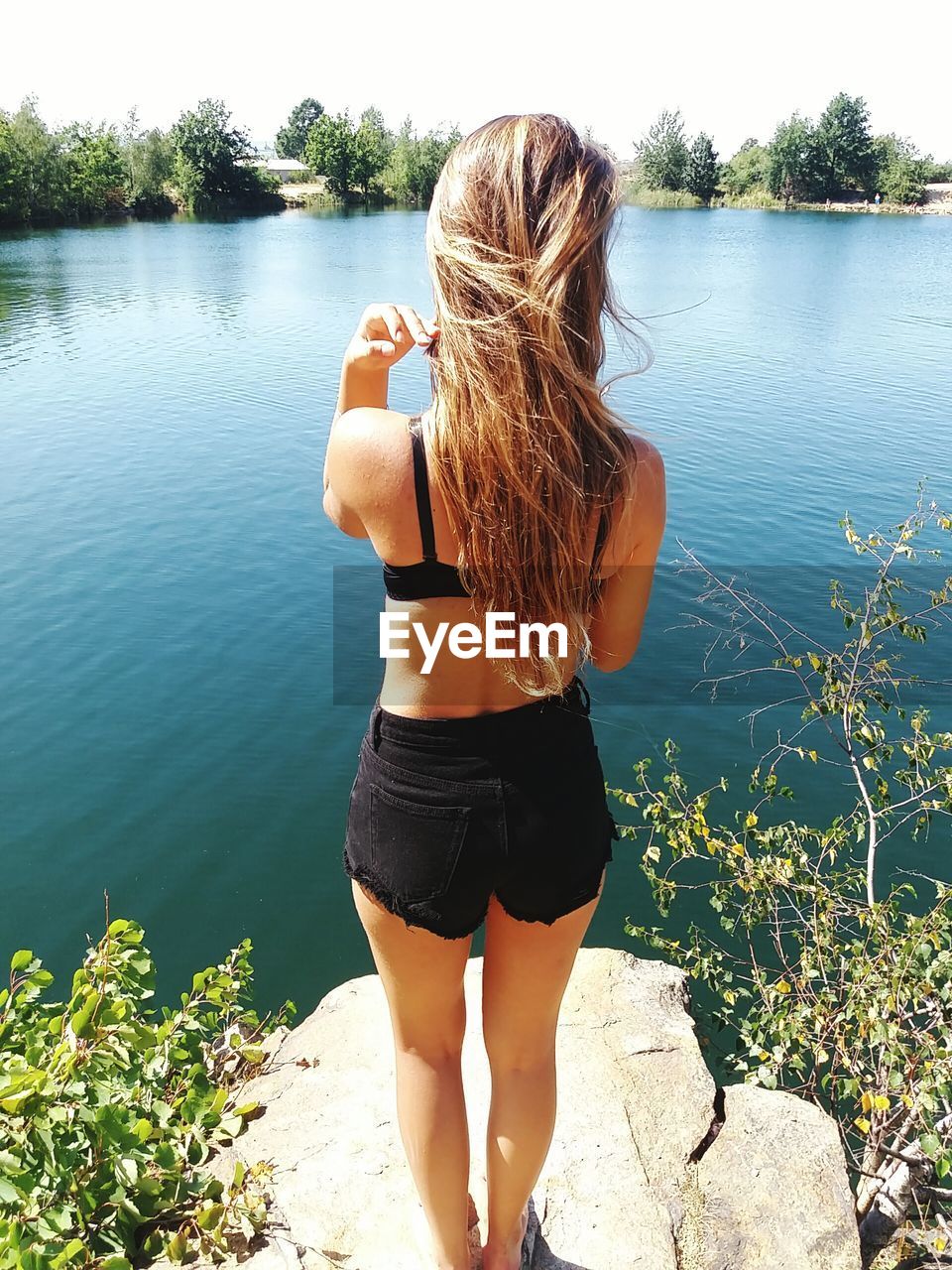 Rear view of young woman standing on rock against lake