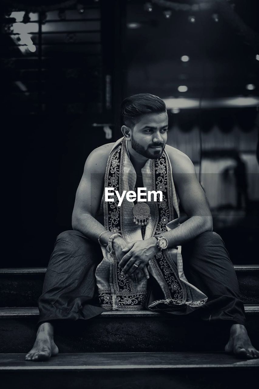 Thoughtful man wearing traditional clothing while sitting on steps