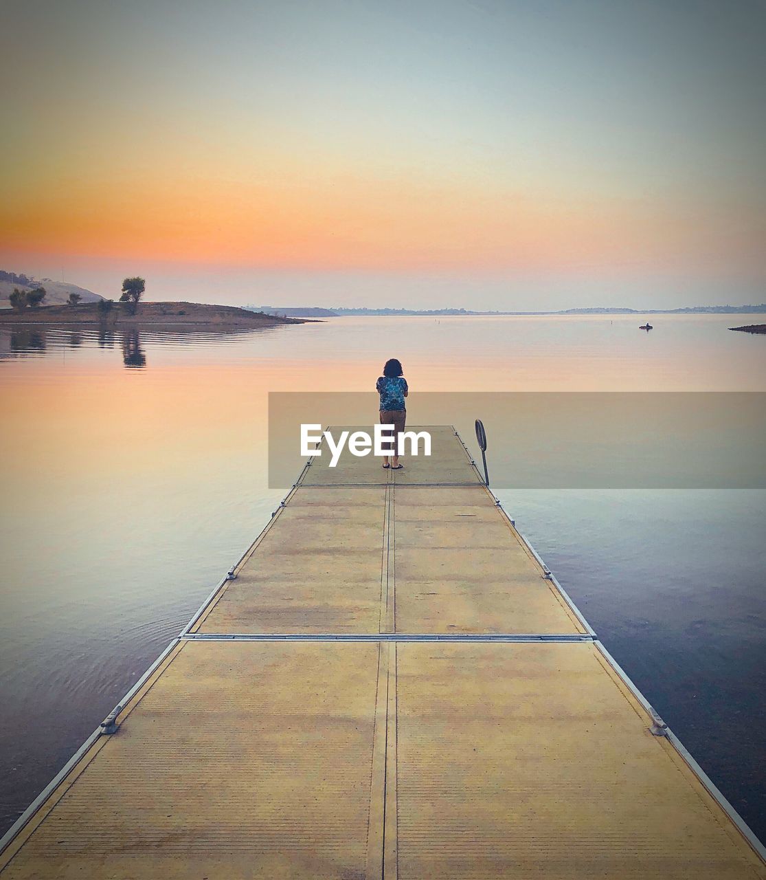 REAR VIEW OF WOMAN STANDING ON JETTY AT SEA AGAINST SKY