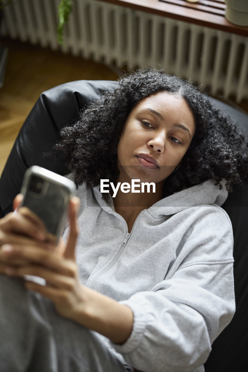 Young woman lying on bean bag and using phone